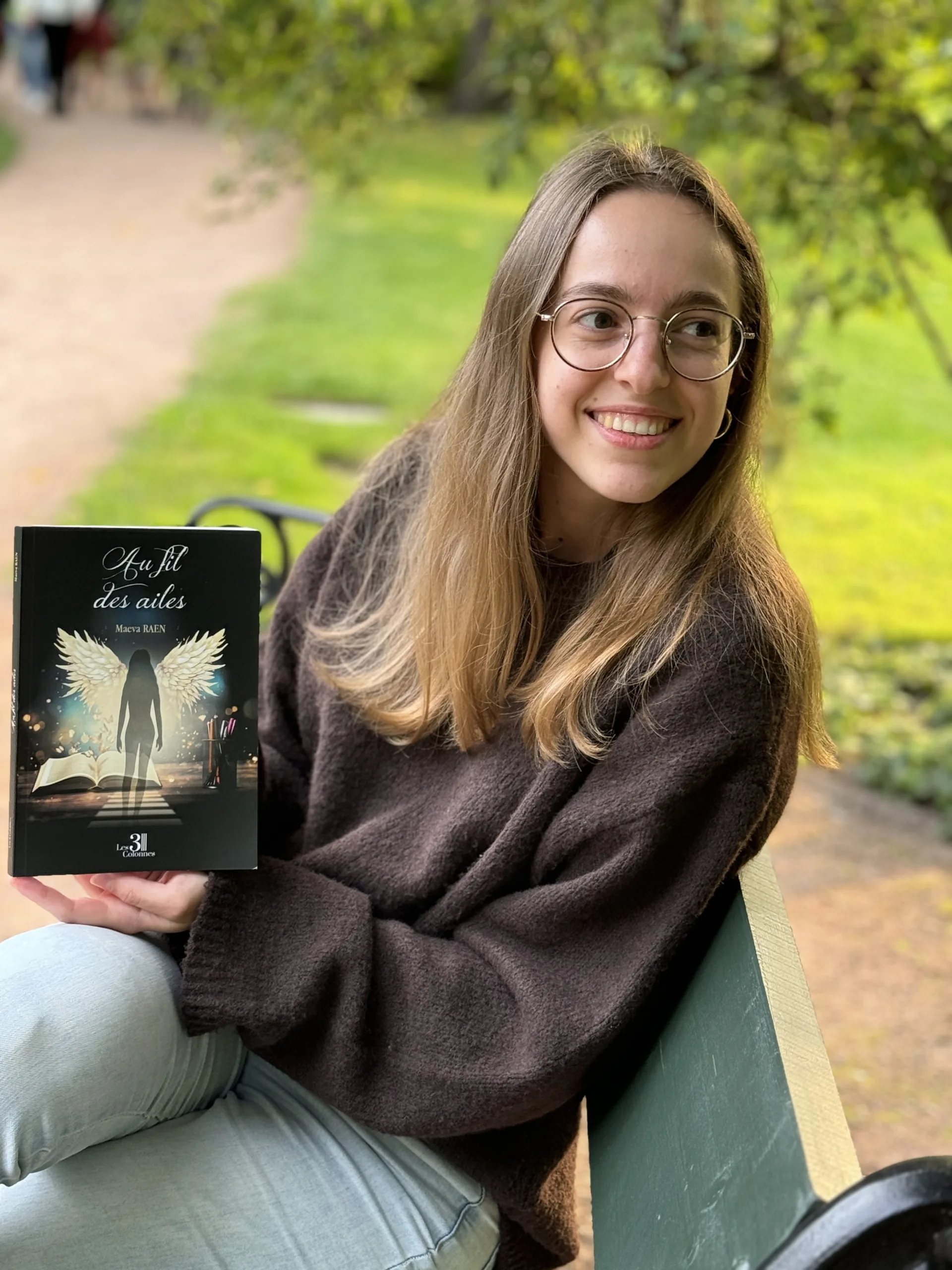 Image de Maeva Raen montrant son livre sur un banc "Au Fil des Ailes"